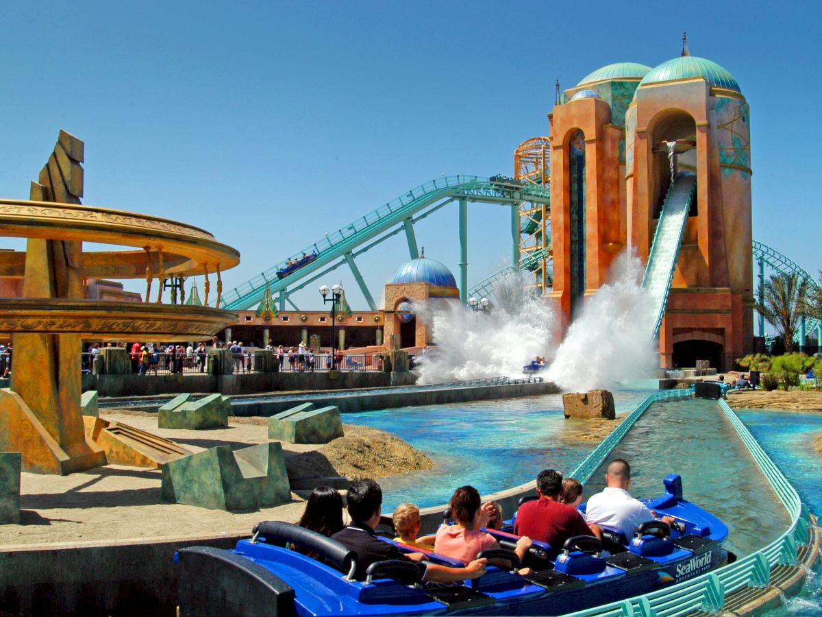 The image shows people on a water ride at an amusement park, with a large splash from the ride and a towering structure in the background.