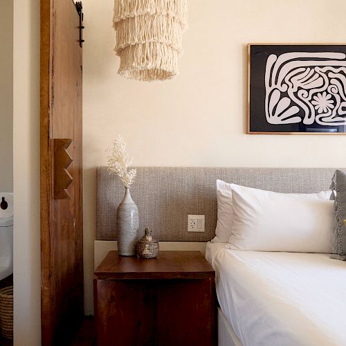 This image shows a cozy bedroom with a bed, wooden nightstand, vase, and decorative light fixture, with a sliding barn door partially open.