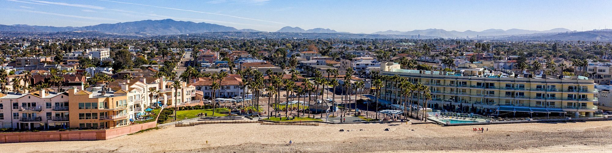 The image shows a coastal town with sandy beaches, waves, buildings, and a mountainous background under a clear blue sky, ending the sentence.