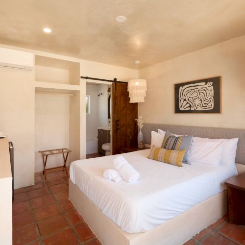 A cozy bedroom with a neatly made bed, TV, air conditioning, and rustic decor, including a framed artwork and pendant lights.