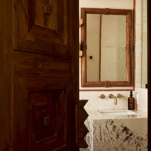 A rustic bathroom with a wooden door, marble sink, and mirrored cabinet; towel rolls and a bottle are on the counter.