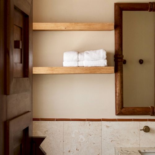 A bathroom with light-colored walls, open shelves holding towels, a framed mirror, a toilet, and a countertop with a towel rack.