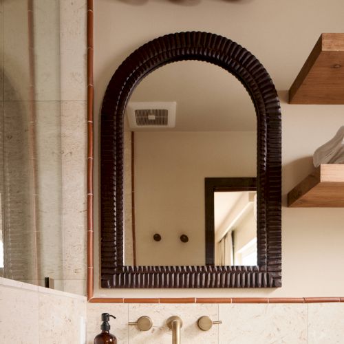 A bathroom scene with a curved mirror, decorative items above, a sink, wooden shelves, and a soap dispenser, creating an elegant and modern look.