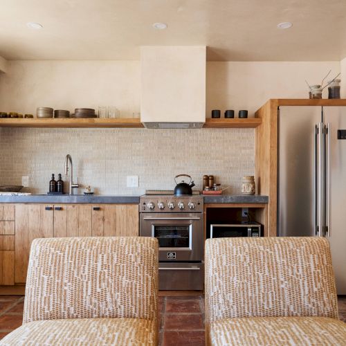 The image shows a modern kitchen with light wood cabinets, stainless steel appliances, a gas stove, and a double-door refrigerator, ending the sentence.