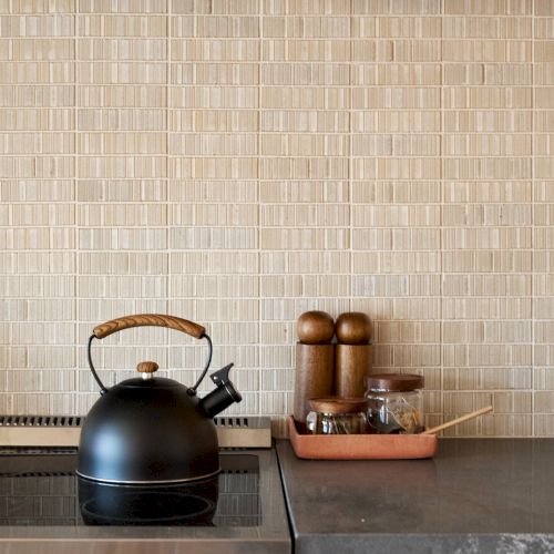 A black kettle on a stove, with salt and pepper grinders, and other condiments on a tray in a modern kitchen setting.