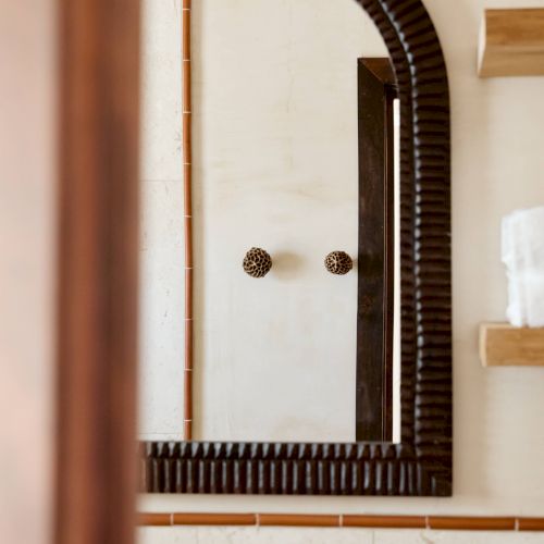 A bathroom with a dark-framed arched mirror, part of a faucet, and a wooden shelf holding white objects are visible in this image.