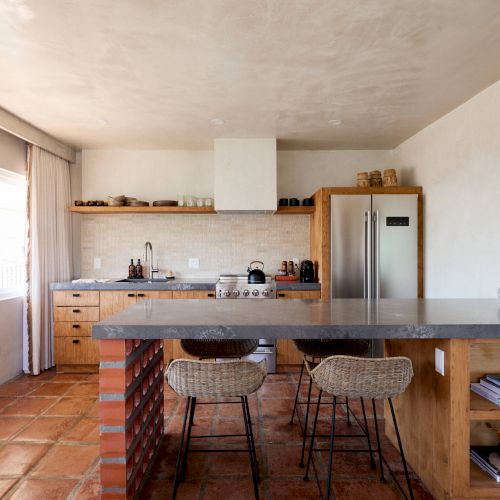 A kitchen with modern farmhouse decor, featuring an island with barstools, open shelving, a refrigerator, and various kitchen accessories.