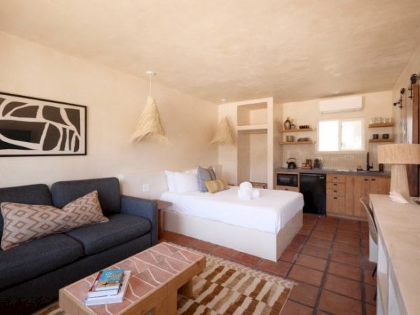 A cozy studio with a bed, sofa, coffee table, kitchenette, and minimalist decor. Earth tones dominate the room, creating a warm atmosphere.