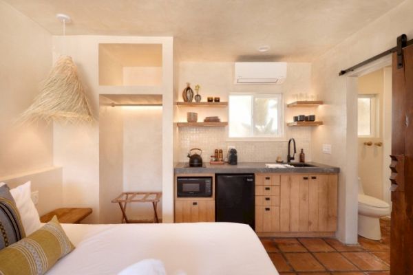 A cozy room with a bed, open shelves, a kitchenette, and a sliding barn door leading to a bathroom; rustic and modern design elements are featured.