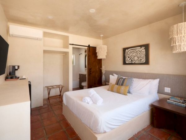 A cozy bedroom with a double bed, wall art, TV, hanging lights, and a small bathroom visible through an open door.