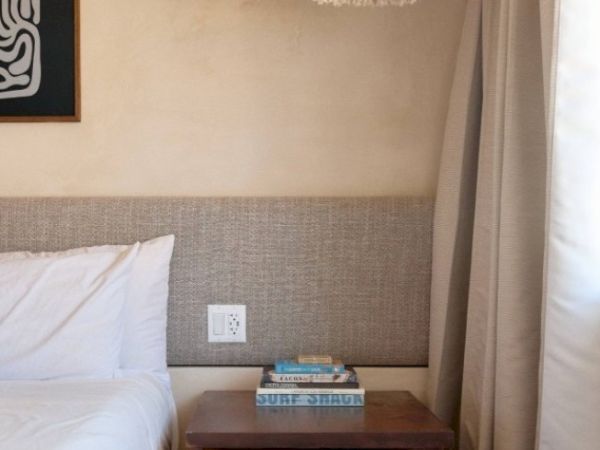 A bedside table with books, next to a bed with a white pillow and gray headboard, and a curtained window nearby ends the sentence.