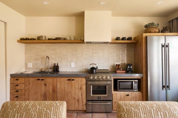 A modern kitchen with wooden cabinets, a stainless steel refrigerator, a stove, a microwave, and open shelves above the counter ending the sentence.