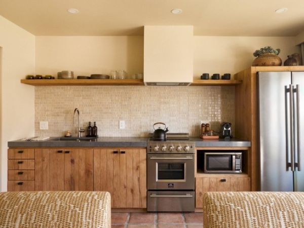 A modern kitchen with wooden cabinets, a stainless steel refrigerator, a stove, a microwave, and open shelves above the counter ending the sentence.