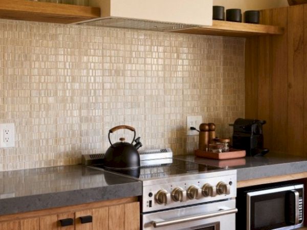A stylish kitchen with wooden cabinetry, a stovetop with kettle, backsplash tiles, microwave, espresso machine, and various kitchen items.
