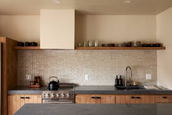 This image shows a modern kitchen with wooden cabinets, a mosaic tile backsplash, open shelving, a stove, and a sink.