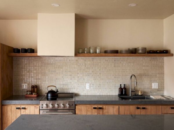 This image shows a modern kitchen with wooden cabinets, a mosaic tile backsplash, open shelving, a stove, and a sink.