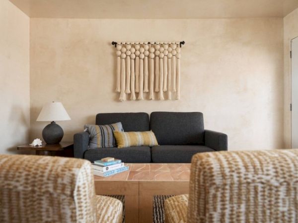 A cozy living room with a dark sofa, patterned armchairs, a lamp on a side table, books on a central table, and wall decor above the sofa.