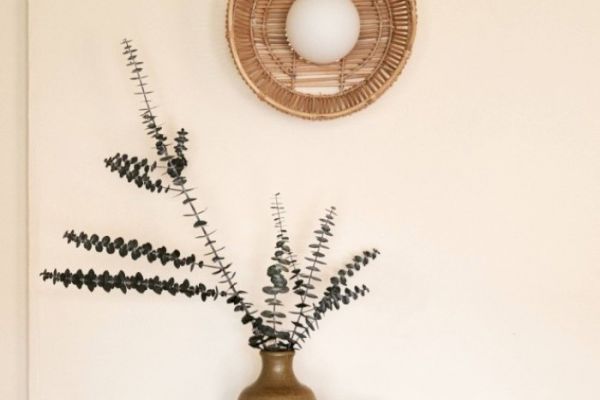 A decorative setup with a rustic vase holding branches of dried foliage, and a woven wall decor with a round white center hanging above it.