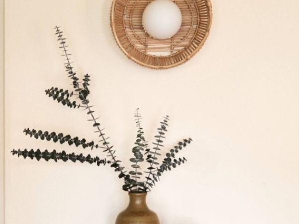A decorative setup with a rustic vase holding branches of dried foliage, and a woven wall decor with a round white center hanging above it.