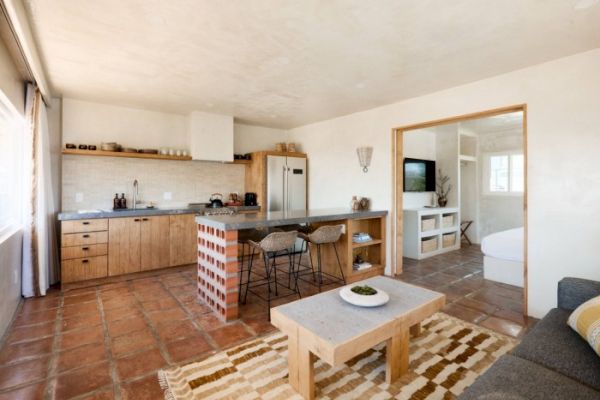 A cozy open-plan living area with a modern kitchen, dining counter with bar stools, wooden coffee table, and a glimpse of a bedroom and bathroom.