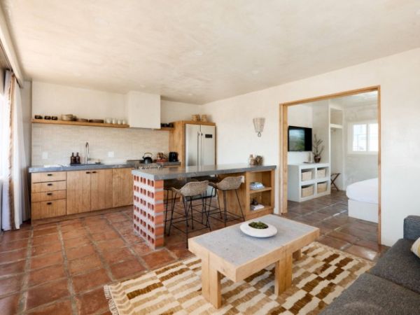 A cozy open-plan living area with a modern kitchen, dining counter with bar stools, wooden coffee table, and a glimpse of a bedroom and bathroom.