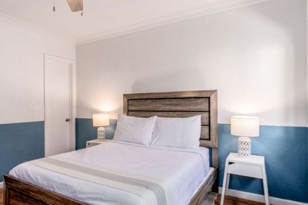 A bedroom with a bed, two side tables with lamps, white and blue walls, and a ceiling fan is shown.