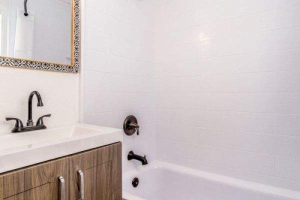 A bathroom with a wooden vanity, a large mirror, a sink with a faucet, and a bathtub with a showerhead and faucet against tiled walls.