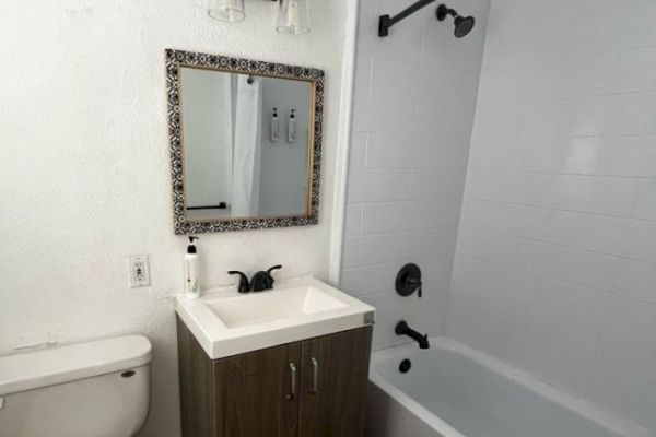 A bathroom with a toilet, a sink with a patterned mirror above it, and a bathtub with a shower curtain and black fixtures, white walls.