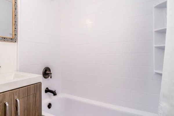 This image shows a modern bathroom with a white bathtub, tile walls, a vanity with a wooden cabinet, and silver fixtures.