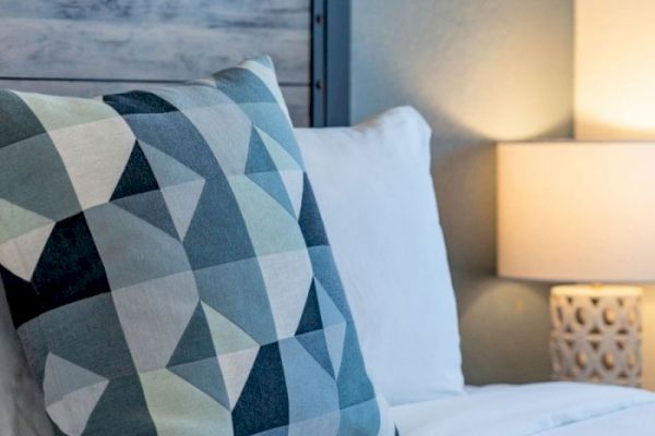 A decorative pillow with geometric patterns on a bed, beside a lit bedside lamp with a carved base.