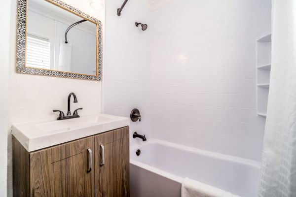 A clean bathroom featuring a sink with a wooden cabinet, a large framed mirror, and a white bathtub with a shower curtain.