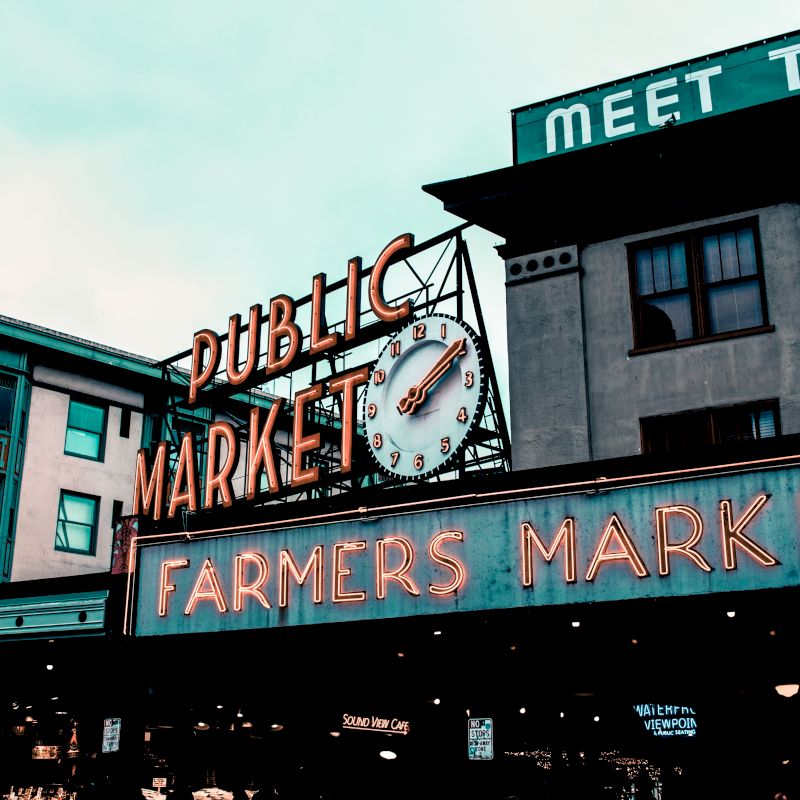 The image features an iconic Public Market and Farmers Market sign with a clock, atop a building in an urban setting.