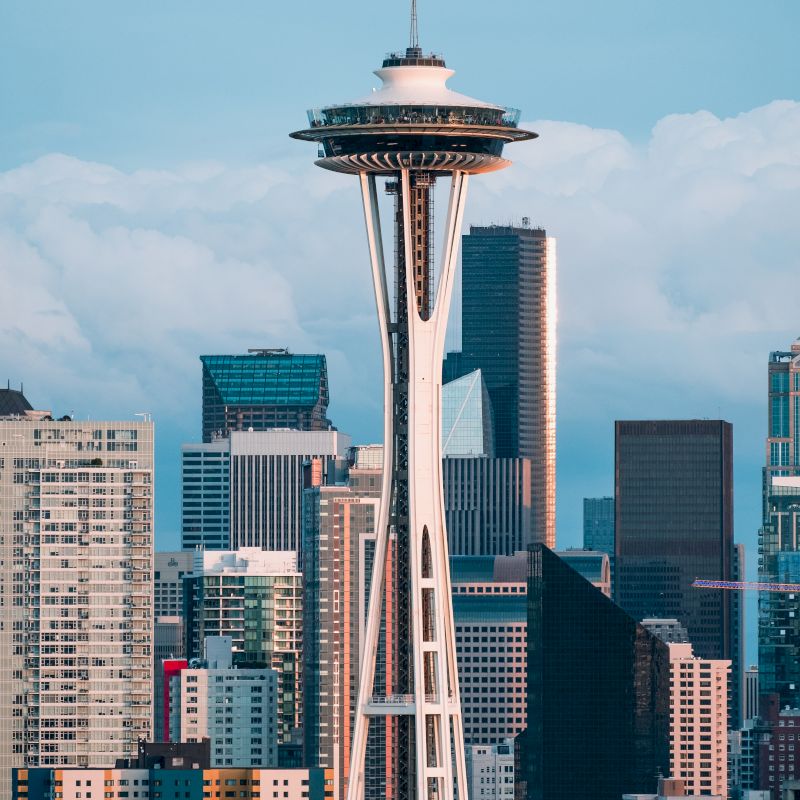 This image depicts the Space Needle, a prominent observation tower, set against the backdrop of a cityscape with several modern skyscrapers.