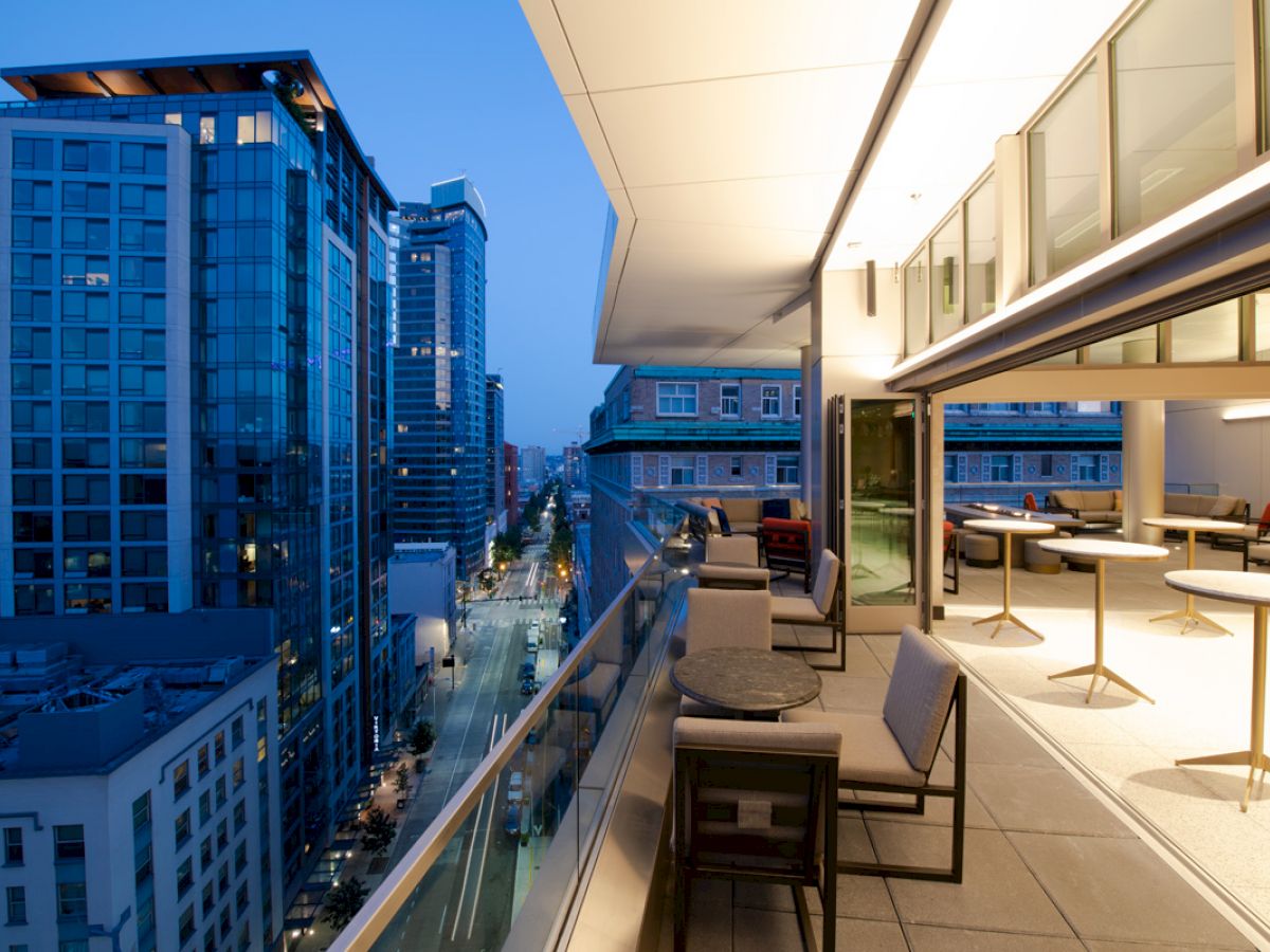 A modern balcony extends from a high-rise building, overlooking a cityscape with tall buildings and streets lit up in the evening.