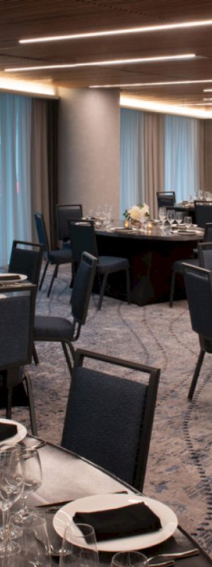 A banquet room with multiple round tables set for an event, featuring black chairs, elegant table settings, flower centerpieces, and candles.
