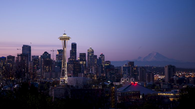 A panoramic view of Seattle's skyline at dusk, featuring the Space Needle and Mount Rainier in the background against a clear sky.