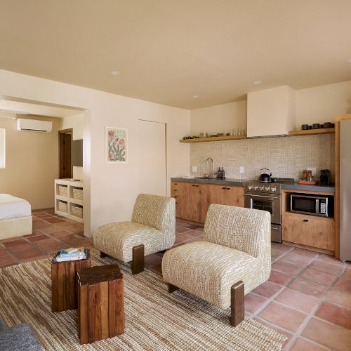 A modern kitchen and living area with a cozy, natural aesthetic featuring wood accents, comfortable seating, and a glimpse of an adjacent bedroom.