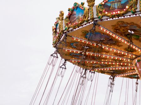 Image of a brightly lit, colorful swing ride at an amusement park, with empty swings hanging and a cloudy sky in the background.